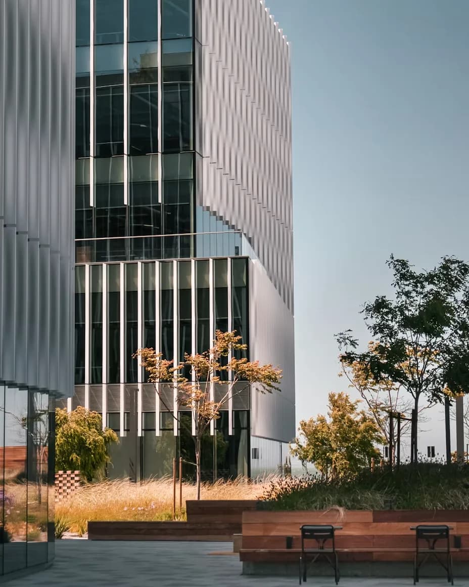 A fluted glass office building above a planted courtyard with benches