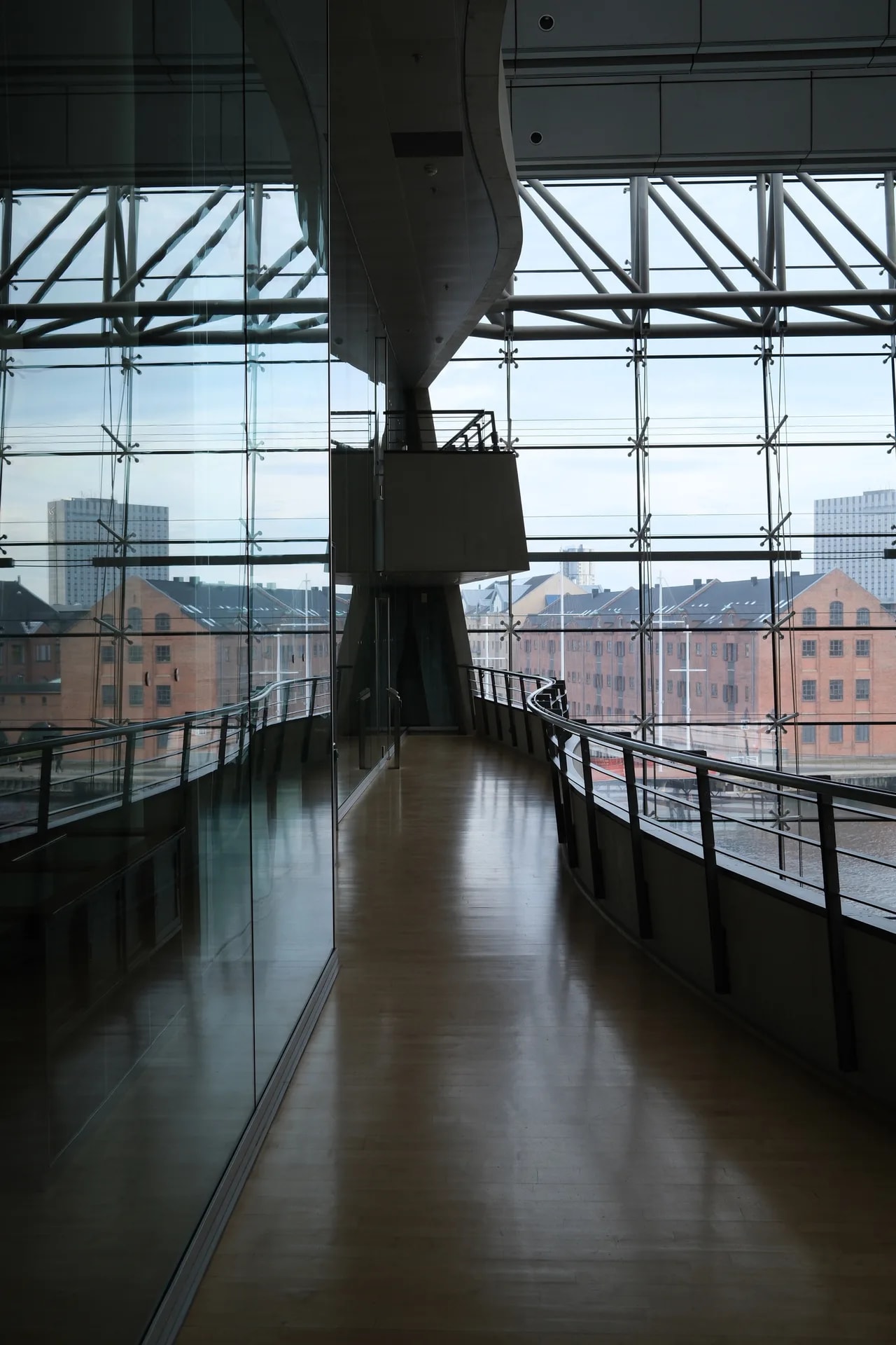 A glass corridor inside the Royal Library with the brick warehouses of the harbour beyond